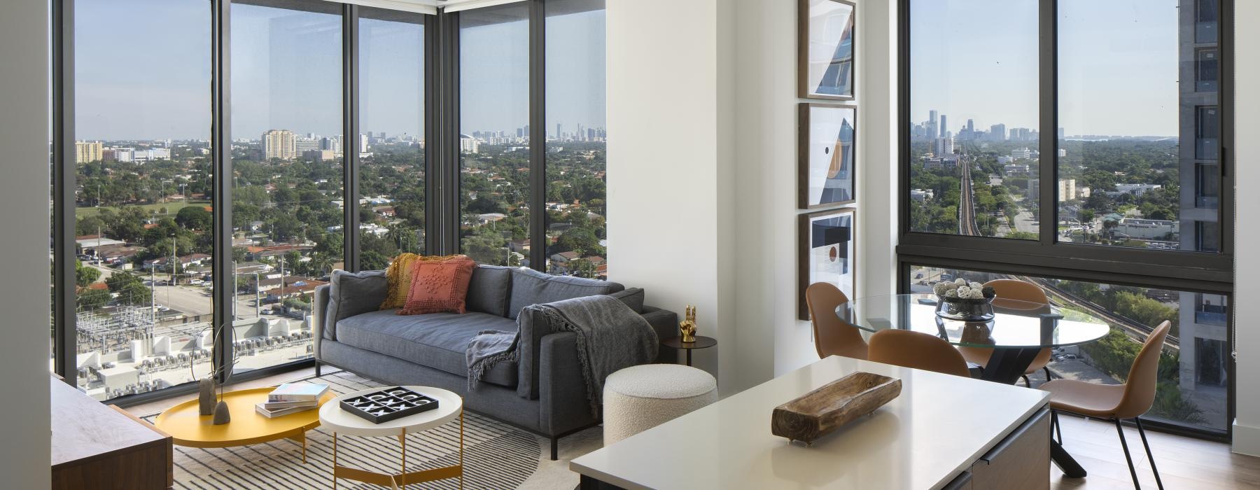 a living room with a couch and a table with chairs and with large windows